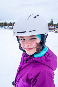Winter outdoor portrait of a cute young girl in ski outfit and white helmet.