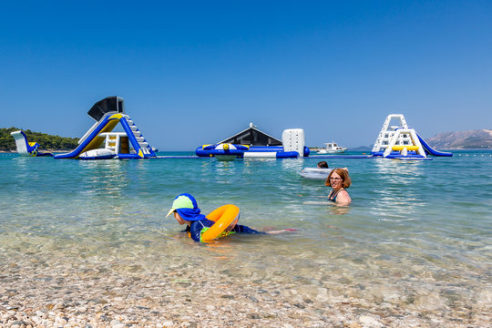 Mother and child swim and having fun in the water with inflatable slides in the background.