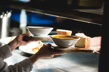 Soup and focaccia being passed from chef to waitress