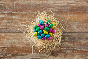 easter, confectionery and holidays concept - chocolate eggs in foil wrappers in straw nest on wooden background