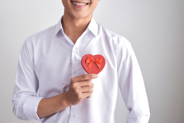 A gift for the beloved. Young beautiful smiling elegant man in a white shirt holding a box with a gift and shows it to the camera. Valentine's Day.