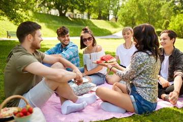 friendship, leisure and summer concept - group of happy friends eating watermelon at picnic in park
