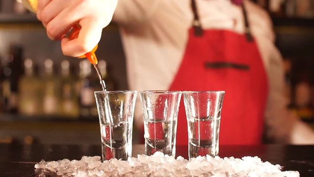 Professional male bartender serving the order, pouring alcoholic drink in a row of shot frozen glasses in a nightclub