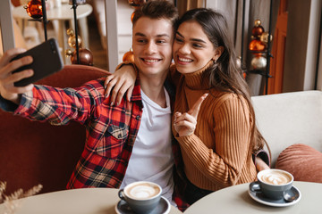 Loving couple sitting in cafe indoors take a selfie by mobile phone.