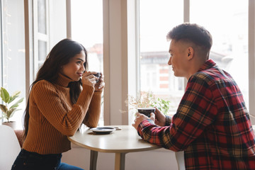 Cute young loving couple sitting in cafe indoors drinking coffee.