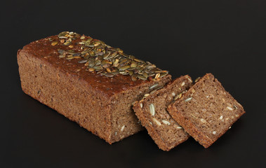Home baked rye bread with sunflower seeds and cut off slices on black background - stacked close up photo on black background