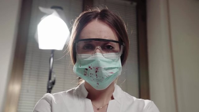 Dentist looking scary and dangerous. Personal or patient mouth point of view POV. Doctor in mask wiht blood and goggles on face. 4K