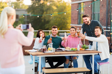 Obraz premium leisure and people concept - happy friends with non alcoholic drinks having dinner party on rooftop in summer and photographing by smartphone
