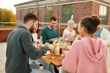 leisure and people concept - happy friends eating at dinner party on rooftop in summer