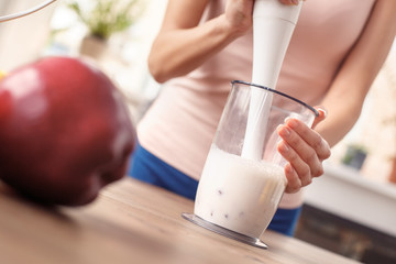 Young girl at kitchen healthy lifestyle standing blending smoothie with hand blender close-up
