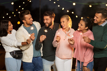 leisure, celebration and people concept - happy friends with sparklers at rooftop party at night