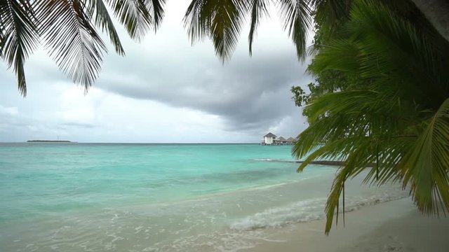 view from beach under pam trees to turquoise ocean with upcoming monsoon sky in a bay lagoon, locked shot