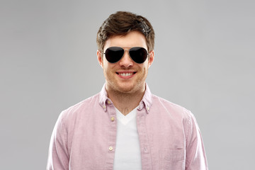 summer, accessories, style and people concept - smiling young man in shirt and black aviator...