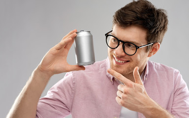drinks and people concept - happy young man in glasses holding tin can with soda over grey...