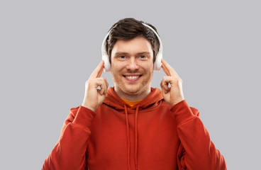 music, technology and people concept - happy young man in headphones and red hoodie over grey background