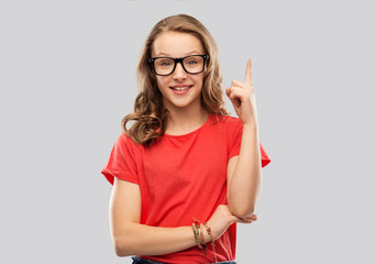 education, school and people concept - smiling teenage student girl in glasses and red t-shirt pointing finger up over grey background