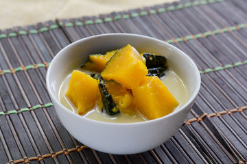 Delicious Thai dessert. Pumpkin in sweet coconut milk in white bowl on wooden table for served after lunch. 
