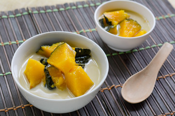 Delicious Thai dessert. Pumpkin in sweet coconut milk in white bowl on wooden table for served after lunch. 