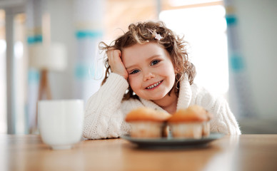 A portrait of small girl sitting at the table at home, eating muffins.