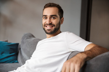 Photo of optimistic man smiling while sitting on sofa in living room