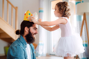 A small girl putting a paper crown on father's head at home when playing.