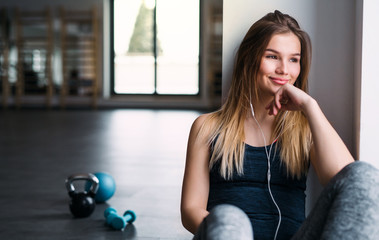 A portrait of young girl or woman earphones in a gym, listening to music.