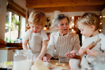 Senior grandmother with small toddler children making cakes at home.
