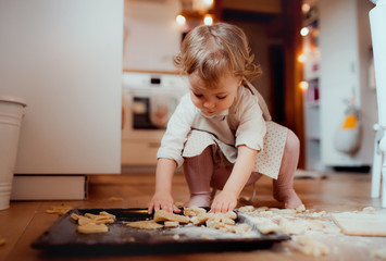 A small toddler girl making cakes on the floor in the kitchen at home.