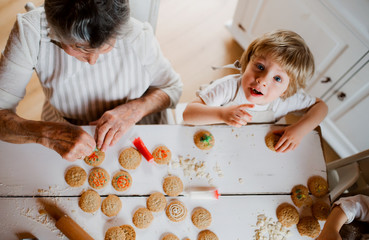 A top view of senior grandmother with small toddler boy making cakes at home.