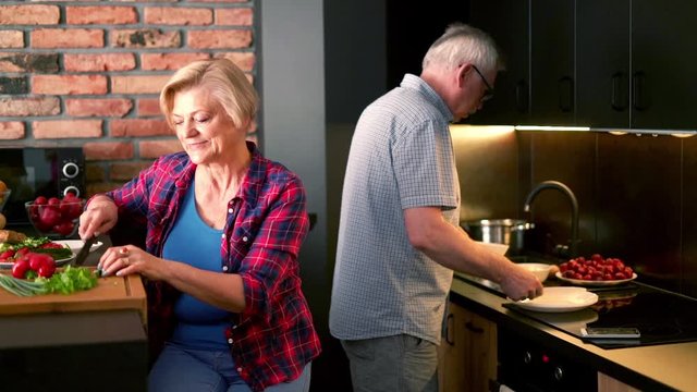 Senior couple preparing salad, woman talking on cellphone 