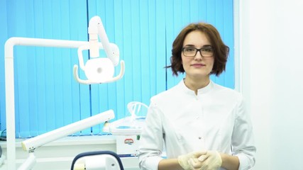 Portrait of a beautiful, young woman doctor wearing medical gloves. Female dental assistant in glasses putting on gloves in dental cabinet.