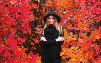 Portrait of a Beautiful girl in dark wear and black hat standing near red autumn leaves. Pretty tenderness model