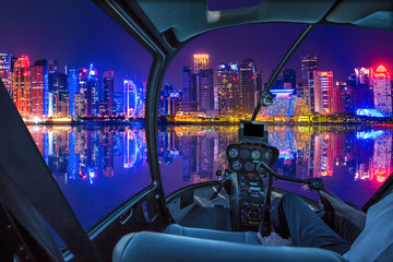 Fototapeta na wymiar Helicopter cockpit interior flying on Skyline of Doha in Qatar in the harbor at blue hour. Night scene waterfront in Doha sea. Qatar, Middle East, Arabian Peninsula in Persian Gulf. Night urban flight