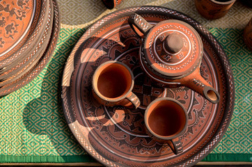 Top view close up of beautiful Gujarati Khavda Pottery earthen terracotta crockery tea cups, kettle and tray at a roadside market exhibition stall on a green mat at Dilli Haat, New Delhi, India