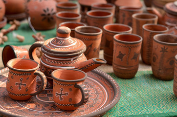Close up of beautiful Gujarati Khavda Pottery earthen decorated terracotta crockery tea cups, kettle and tray with glasses at a roadside market exhibition stall at Dilli Haat, New Delhi, India