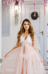 Fototapeta premium Cute girl in soft pink negligee poses in a spring studio