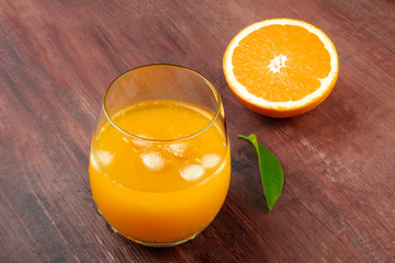 A glass of fresh orange juice with an orange half and a green leaf on a dark rustic wooden background with copy space