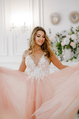Fototapeta na wymiar Amazing girl in a pink-white dress posing in a refined hall