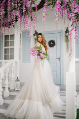 Fototapeta premium Luxury girl in a long white dress standing on the stairs with a bouquet in her hands