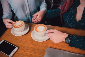 Closeup image of two people's hands holding coffee cups on wooden table in cafe.