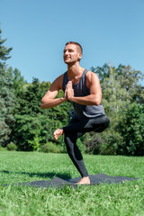 Healthy Lifestyle. Man practicing yoga on mat outdoors in one legged prayer pose cheerful