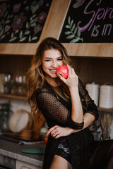 Comely girl in black dress holding a red apple in her hand. The girl poses in the kitchen