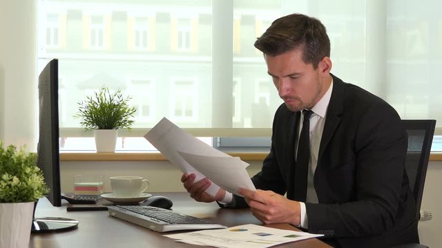 An office worker in a suit works on a computer and reads papers for work