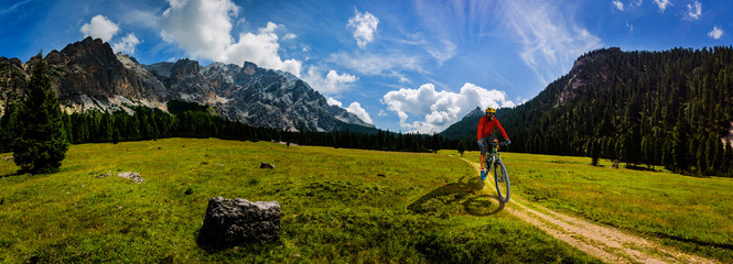 Tourist cycling in Cortina d'Ampezzo, stunning rocky mountains on the background. Man riding MTB enduro flow trail. South Tyrol province of Italy, Dolomites.