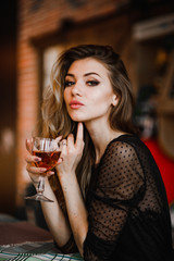 A sexy blonde holds a glass of cognac in her hand