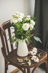 Spring white buttercup flowers in enamel jug on wooden vintage chair with white wall and black curtain at background. Wedding bouquet, flower shop, Womens Day holiday or spring mood concept