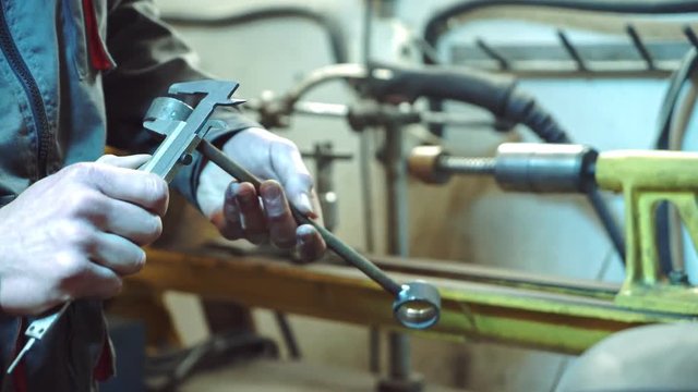 A mechanic in working form and gloves measures height, width and length of the ball joint for a car on the background of the service room. Close-up.