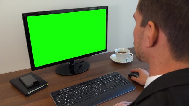An office worker in a suit works on a computer with a green screen - closeup