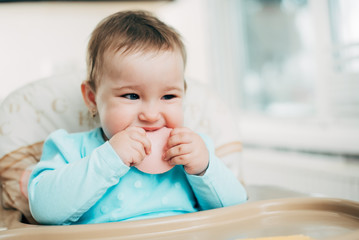 Fototapeta premium a little girl in a high chair eating a piece of boiled sausage