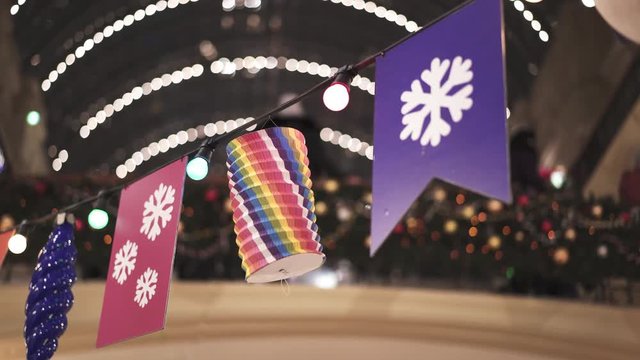 Handheld pan shot from left to right of different colorful flags hanging on wire with lamps inside department store. Different Christmas decorations hanging indoors in store